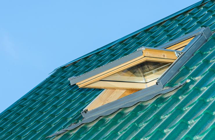 Dachfläche mit grünem Ziegeldach und geöffnetem Dachfenster unter klarem Himmel.